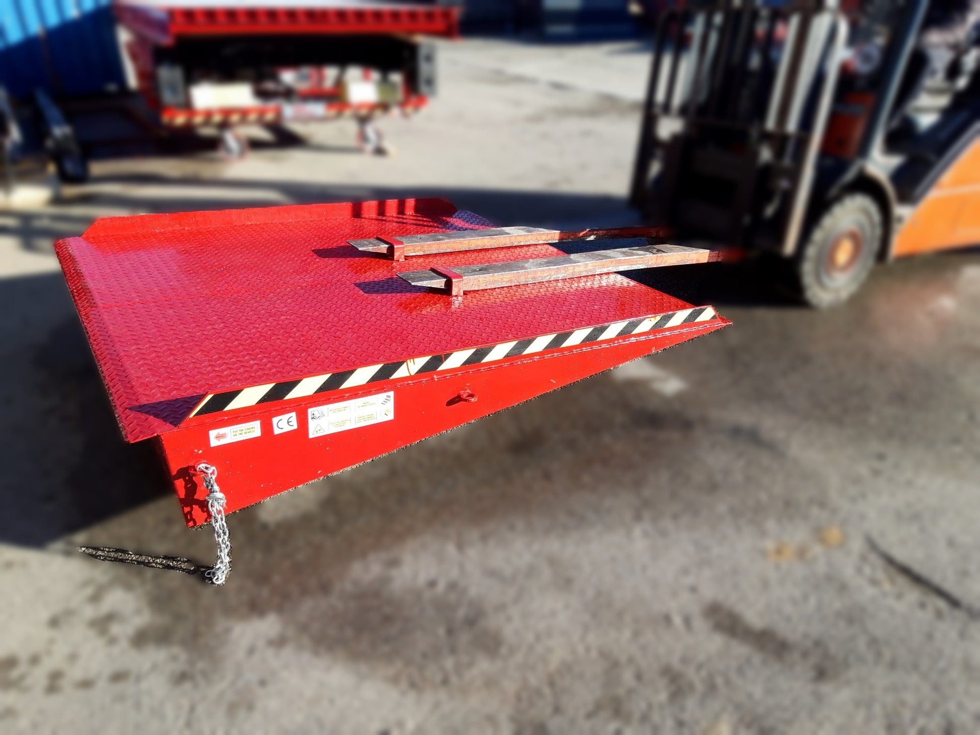  Rampa de acceso móvil para contenedor de residuos en el suelo, siendo desplazada. Capacidad: 8,000 Kg. Dimensiones: 2,000 x 2,000 x 300 mm. Peso: 295 Kg. Ideal para carga/descarga rápida con cualquier equipo de manipulación. Se desplaza fácilmente con calces de horquilla.